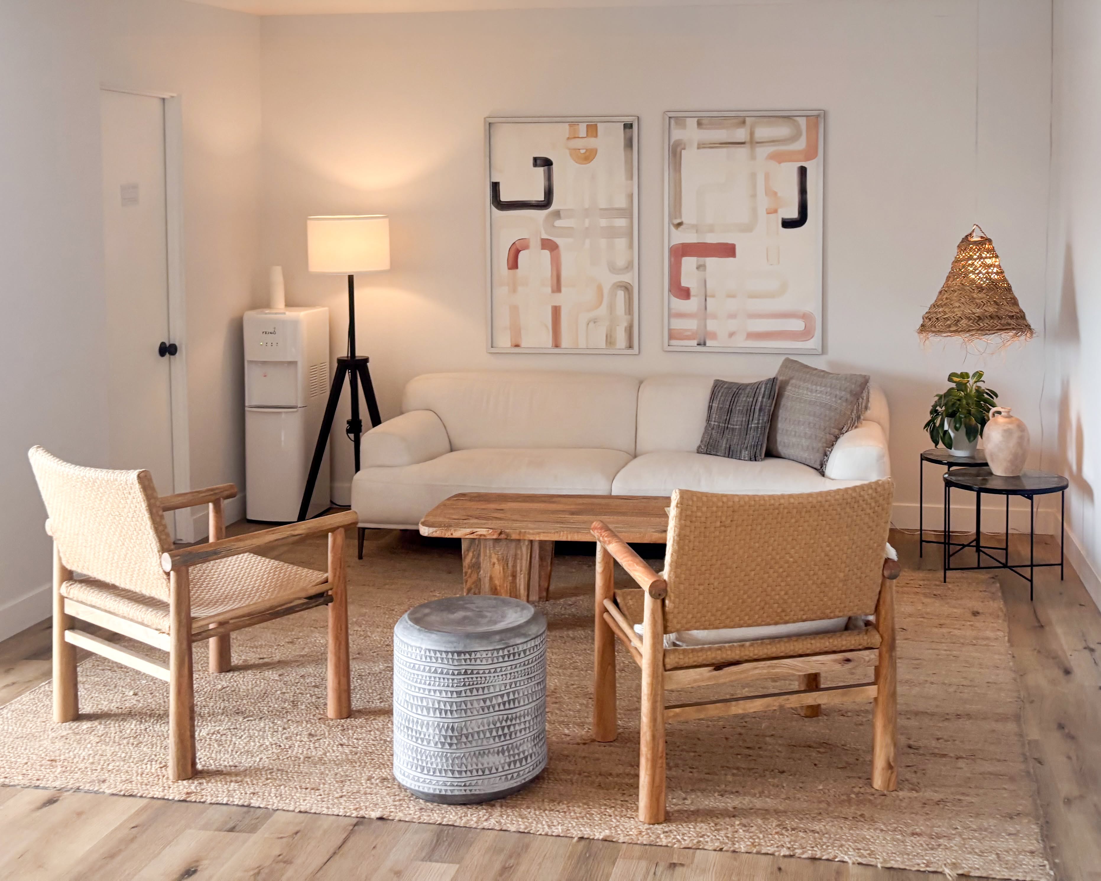 A calm, naturally lit office with a sofa and two woven armchairs facing a low wood table.